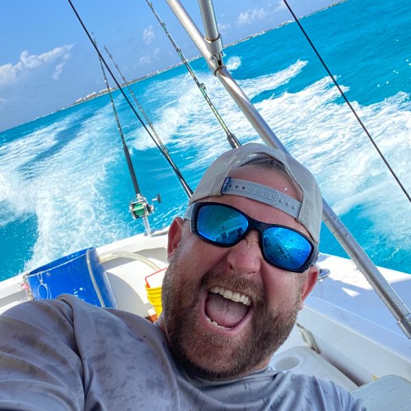 a man wearing sunglasses and sitting in a boat on a body of water