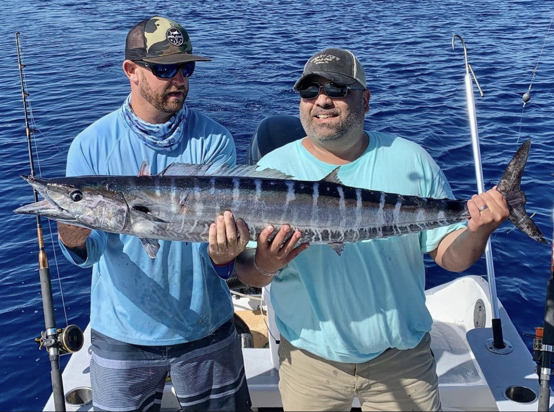 wahoo Two anglers holding a large wahoo on a boat during a fishing charter in Cancún.